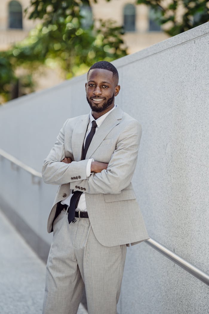Smiling Man in a Gray Suit Standing with Arms Crossed by a Fence
